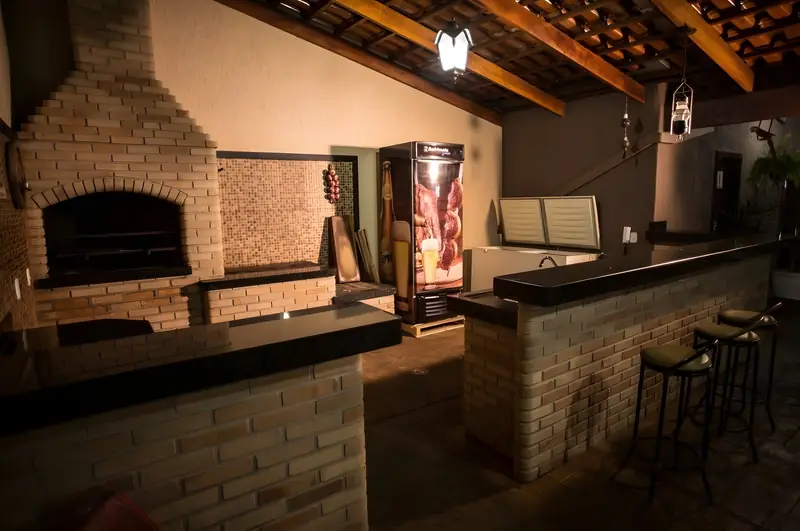 Área gourmet com churrasqueira, balcão de bar em granito e banquetas