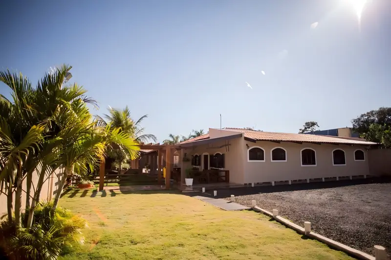 Casa das suítes com janelas em arco, gramado e palmeiras em dia de sol