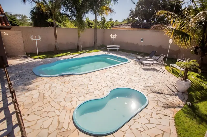 Vista das duas piscinas, adulto e infantil, com deque de pedra e espreguiçadeiras