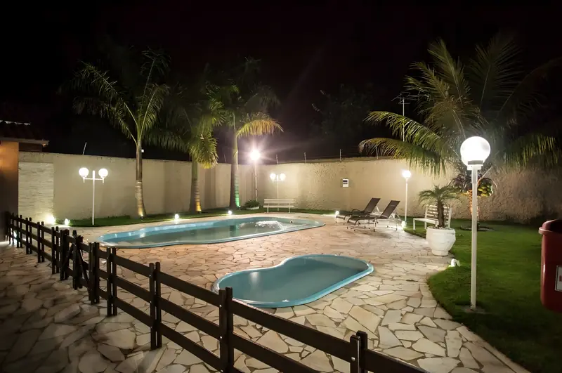 Piscina adulto e piscina infantil iluminadas à noite, com luminárias e palmeiras