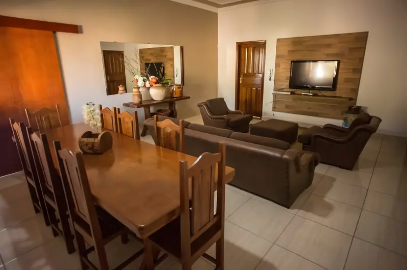 Sala de estar com sofás e TV em painel de madeira e mesa de jantar de madeira