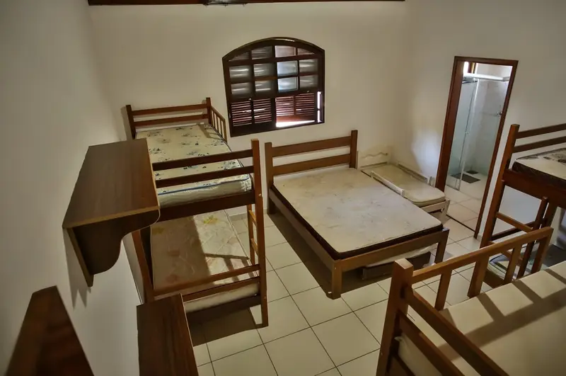 Suíte com beliches, cama de casal e banheiro com box de vidro ao fundo